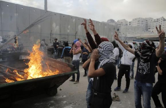 Palestinian stone-throwers gesture in front of garbage set ablaze during clashes with Israeli police on outskirts of Jerusalem