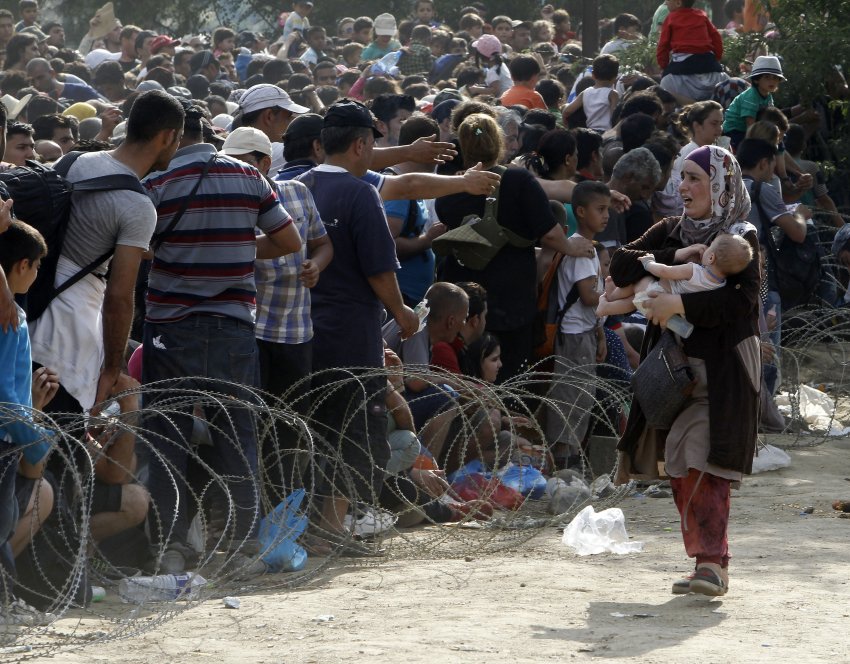 A woman migrant, right,  with a baby looks for her family in the crowd of migrants waiting to enter Macedonia passing the police blockade set at the railway tracks on the border line with Greece, near the southern Macedonia's town of Gevgelija, on Friday, Aug. 21, 2015. About 39,000 people, mostly Syrian migrants, have been registered as passing through Macedonia in the past month, twice as many as the month before. They previously encountered little resistance at the border, but the recent influx has overwhelmed Macedonian authorities who this week declared a state of emergency and stopped many from crossing. (AP Photo/Boris Grdanoski)
